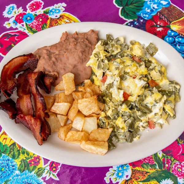 A breakfast plate with scrambled eggs and nopales, bacon, home fries, and refried beans.