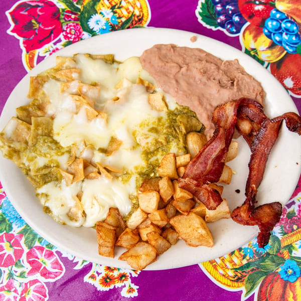Chilaquiles with green salsa and melted cheese, served with refried beans, home fries, and bacon.